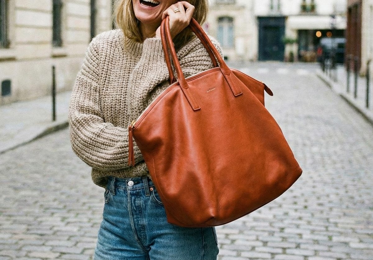Woman holding a brown leather zippered tote bag on a city street