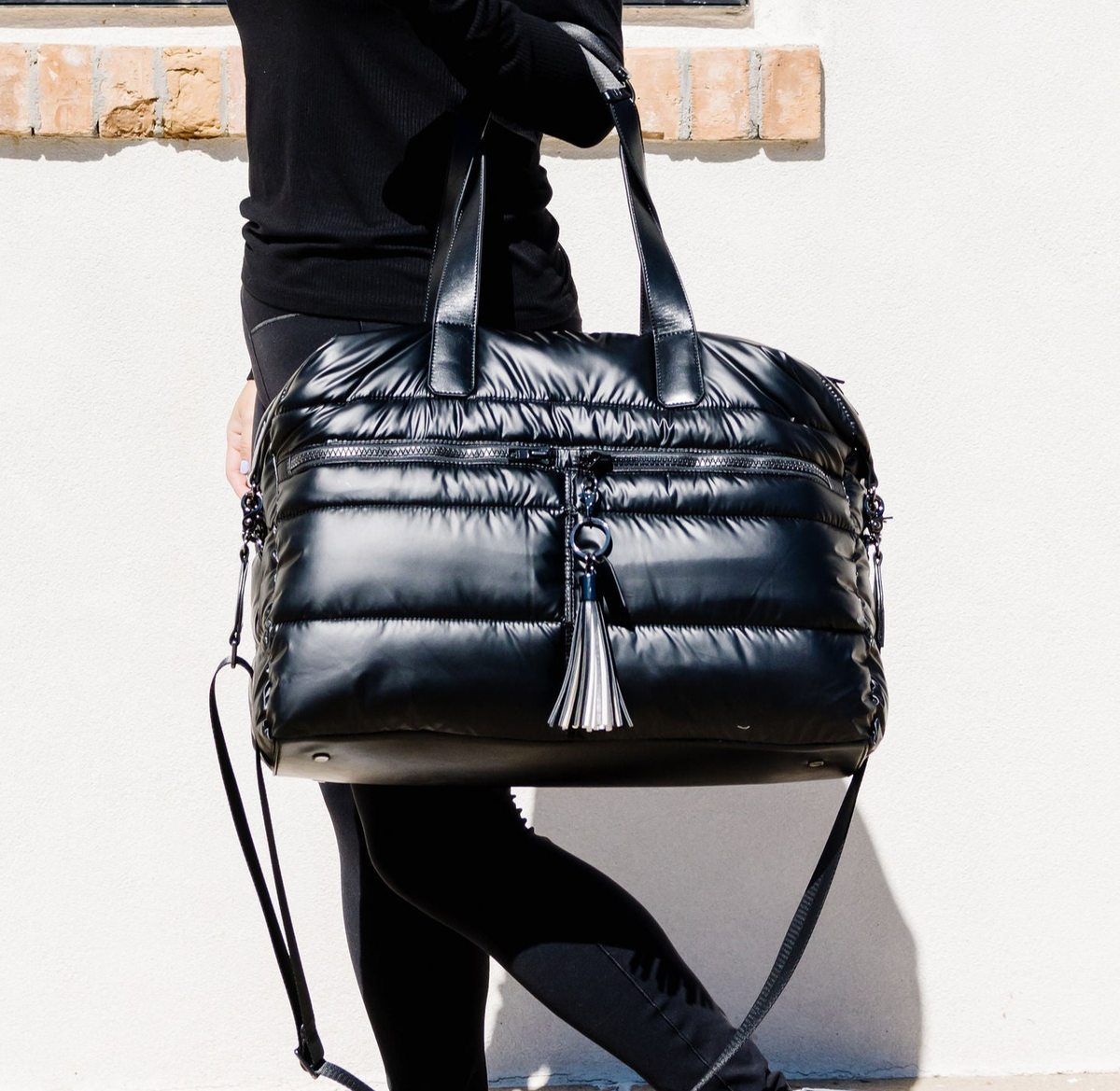 A black puffer tote hanging from a person's arm, against a white background.