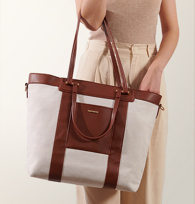 Tan and brown canvas diaper bag hanging from a persons arm.