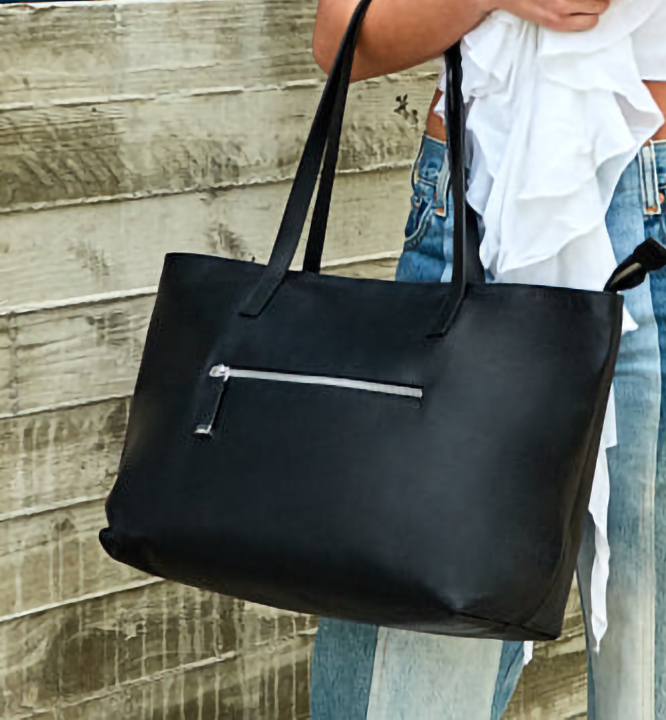 A black leather tote with a zipper in the front hangs from a person's arm.