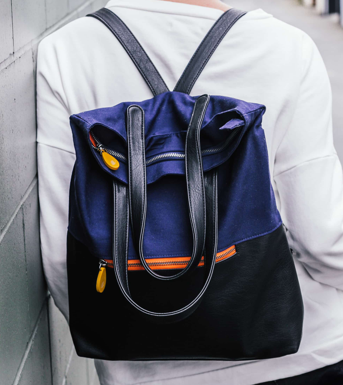 Navy and black vegan convertible backpack tote on a person's back.