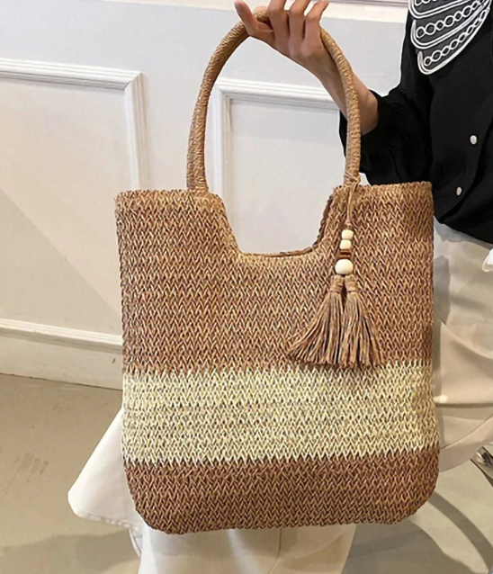 A person's hand holding a woven tote bag with a long handle and made from tan woven material.