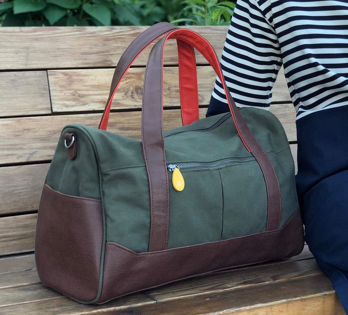 A green and brown zip-top tote on a bench next to a person.