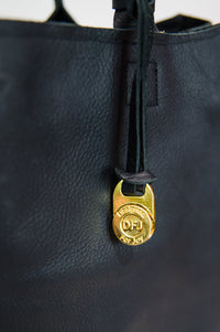 Black leather tote with a removable gold lock featuring 'DFJ' branding.