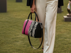 Woman in formal attire with a black blazer and white pants, holding a pink, black and animal print tote, at an outdoor event.
