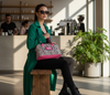 Woman in a green coat holding a pink and zebra-striped tote in a cafe setting
