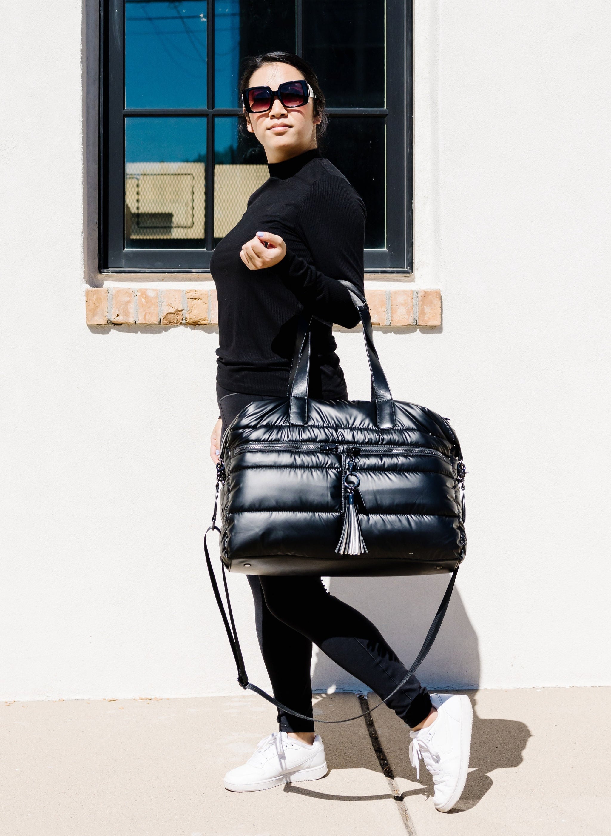 Woman holding a black quilted handbag in front of a building