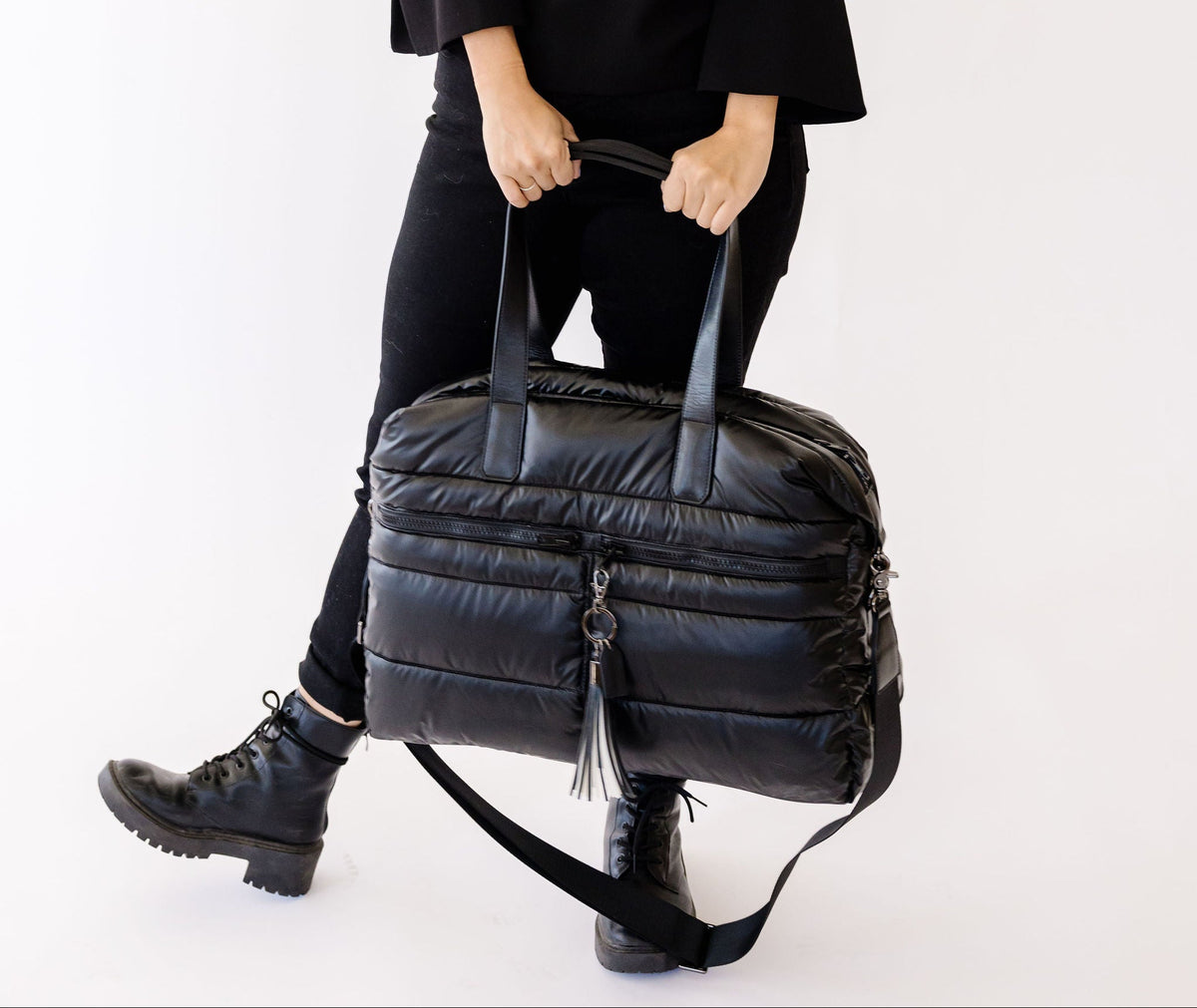 Woman holding a black puffer weekender tote bag against a white background