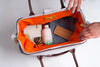 Person packing items into an open suitcase with an wire frame and orange interior.