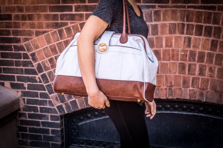 Person holding a stone gray weekender tote against a brick wall.