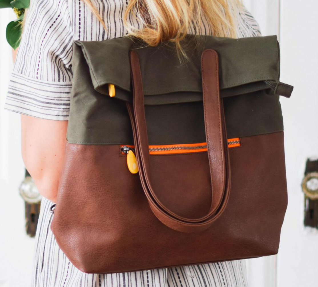 Person holding a brown and green convertible tote backpack with orange accents.