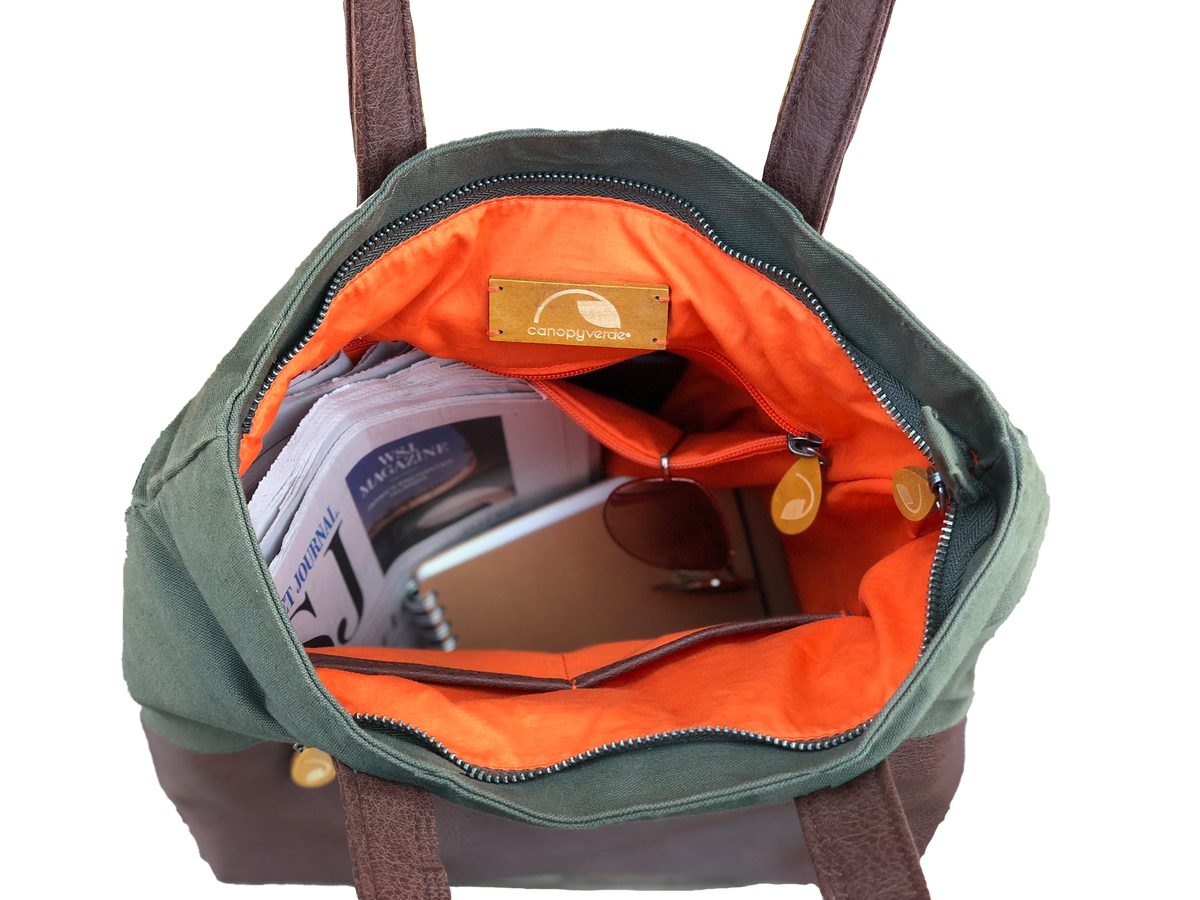 Green convertible tote backpack with orange interior, showing a brand label, on a white background