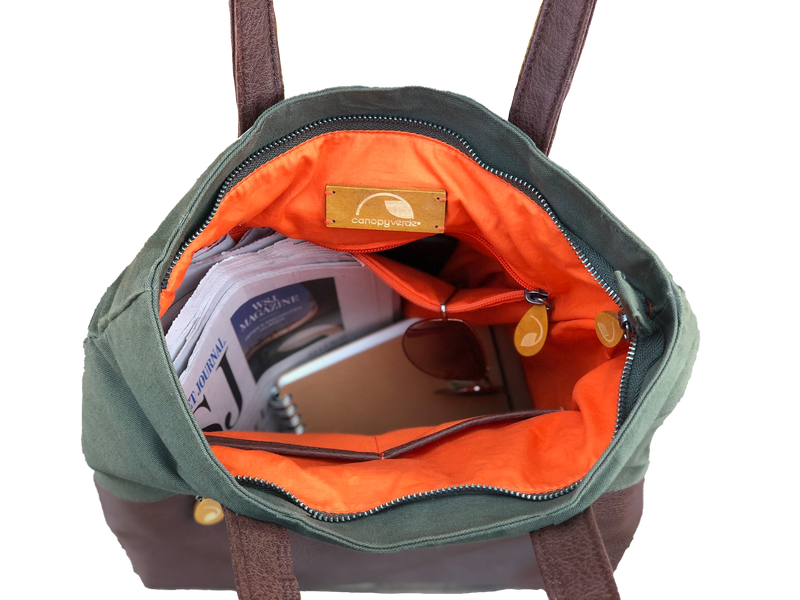 Green convertible tote backpack with orange interior, showing a brand label, on a white background