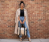 Woman in a beige coat and blue jeans holding a gold puffer laptop tote against a brick wall.