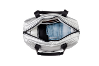 Silver puffer tote bag with black straps containing a blue denim jacket on a white background