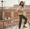 Woman walking outdoors with a scenic background holding a gold tote