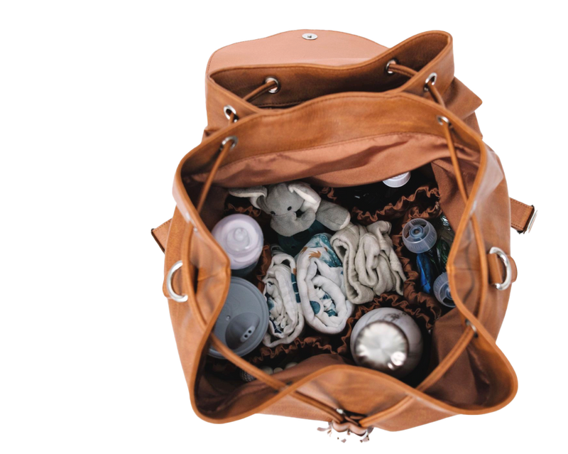 Brown vegan leather convertible backpack diaper bag with baby items including diapers and bottles on a white background