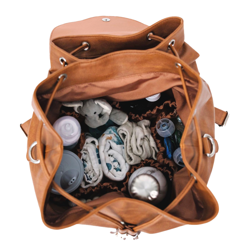 Brown vegan leather tote, open with baby items including bottles and blankets on a white background