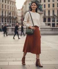 Woman in a white sweater and brown pleated skirt carrying a green puffer tote and standing in an urban setting