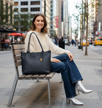 Woman sitting on a bench in an urban setting with a black leather tote bag.