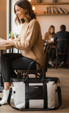 Woman using a laptop at a cafe with a convertible diaper bag canvas tote on the floor