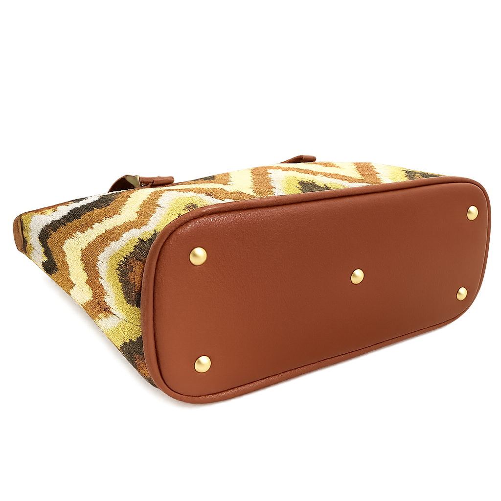 A chevron-pattern kilim woven tote with a brown bottom is laying on its side