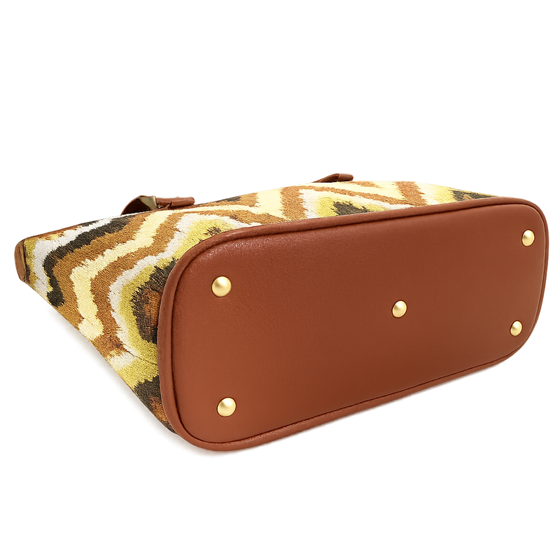 A chevron-pattern kilim woven tote with a brown bottom is laying on its side