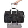 Hand holding a black patterned diaper tote with a luggage sleeve, attached to a luggage handle.