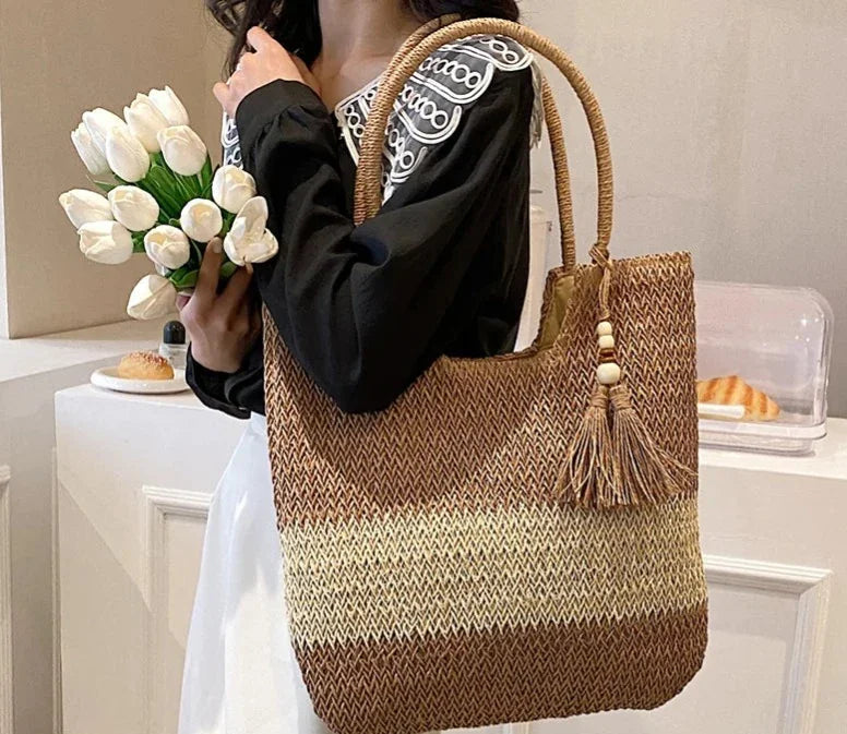 Person holding a woven tote with a tassel, standing in a casual setting.