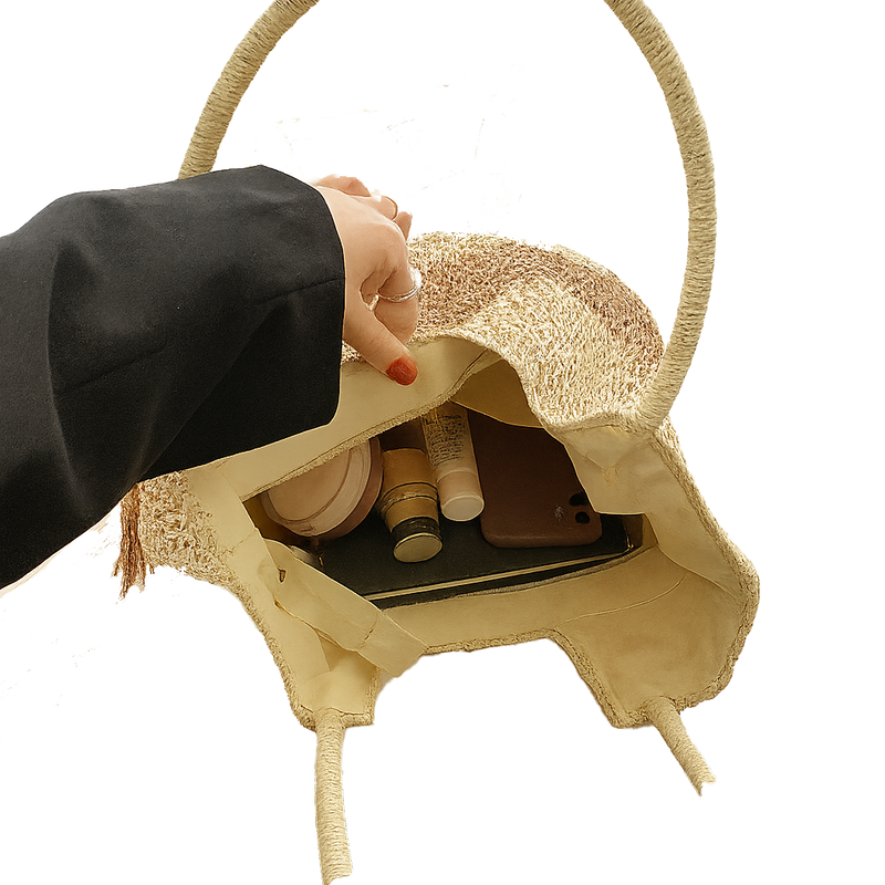 Hand opening a tan woven tote with cosmetic items on a white background