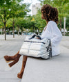 Person sitting on a bench with a silver puffer tote bag in an urban setting