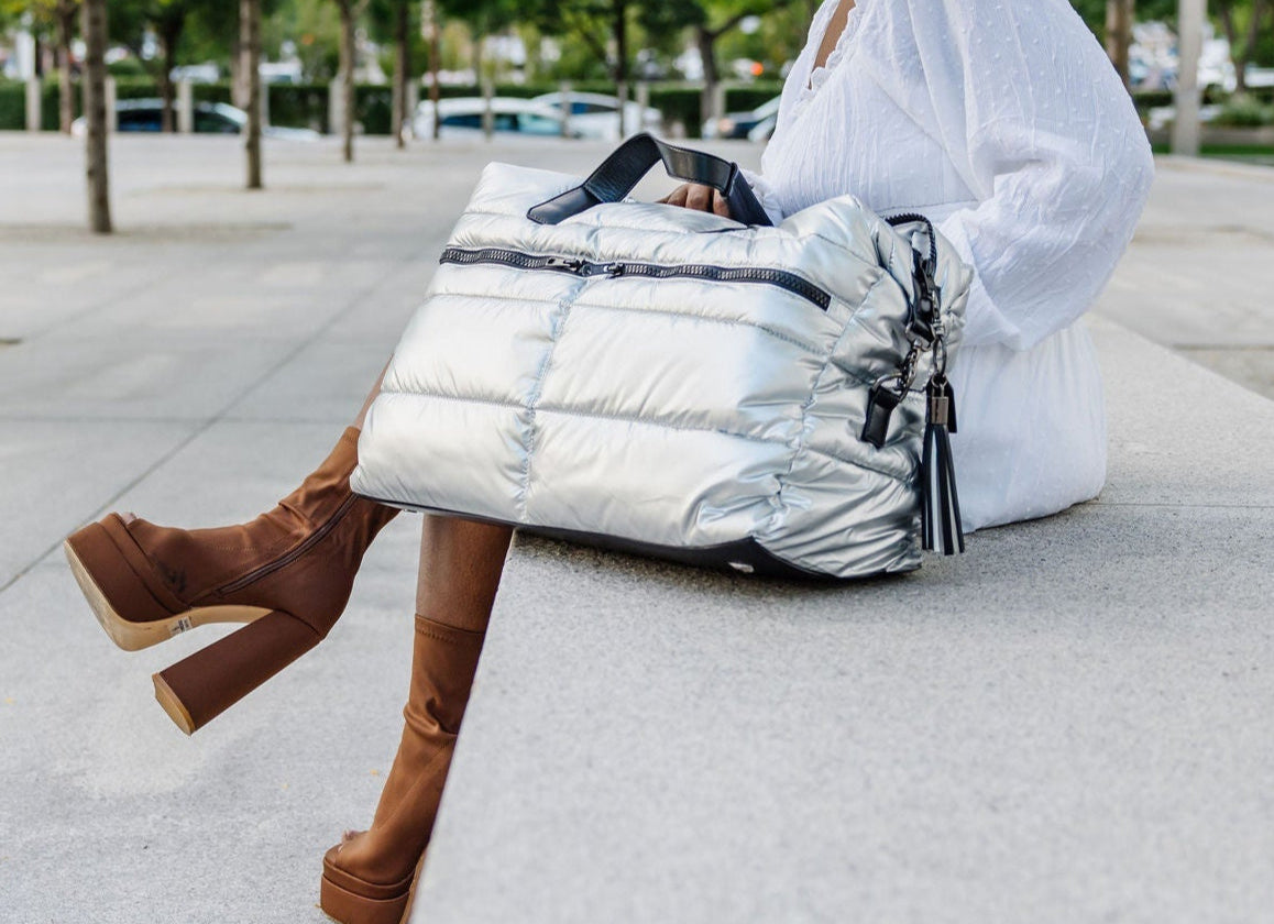 Person sitting on a bench with a silver puffer bag in an urban setting
