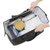 Black patterned diaper bag tote with contents including a yellow container and blue item, held open by hands.