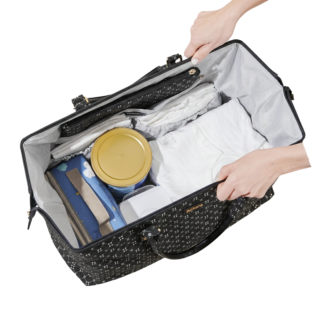 Black patterned diaper bag tote with contents including a yellow container and blue item, held open by hands.