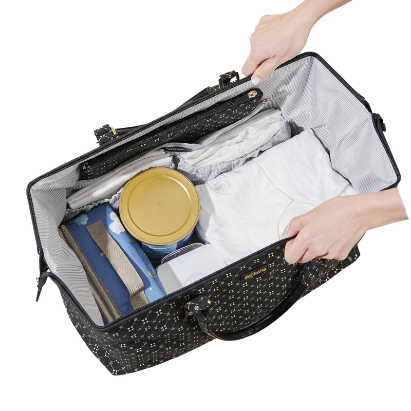 Black patterned diaper bag tote with contents including a yellow container and blue item, held open by hands.