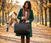 Woman in a green coat holding a black handbag in an autumn park.