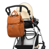 Brown leather backpack attached to a baby stroller on a white background