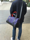 Person carrying a blue duffel bag with black straps on a sidewalk