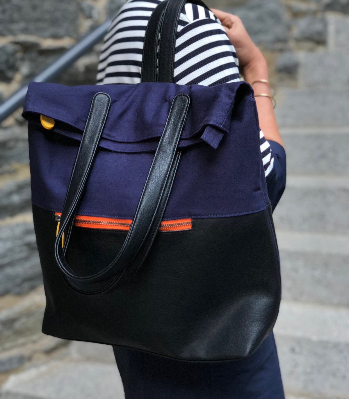 Person wearing a navy navy and black convertible tote backpack with orange accents, standing on stone steps.