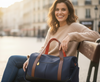 Woman sitting on a bench holding a blue duffel bag with brown handles in an urban setting.
