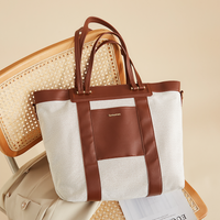 Canvas convertible diaper bag tote with brown straps on a beige surface