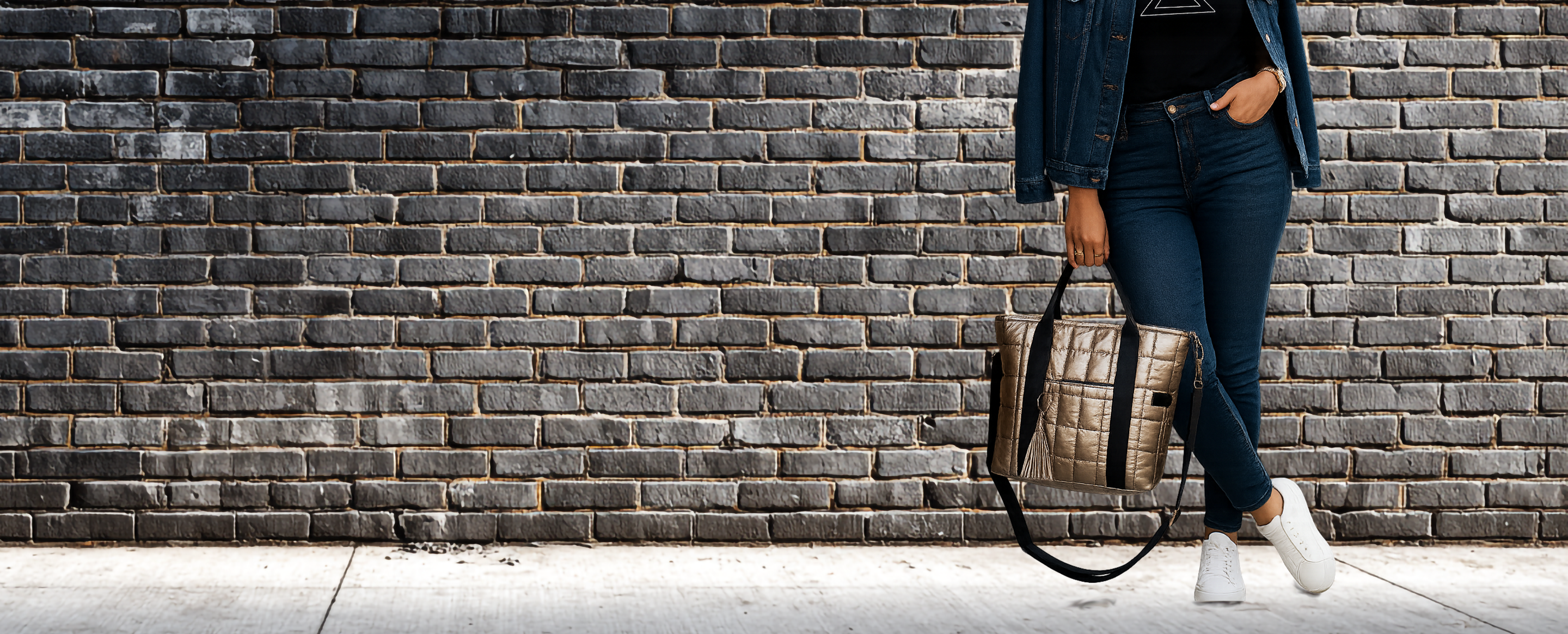 Woman holding a gold laptop tote against a brick wall