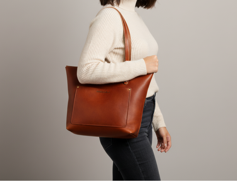 Woman holding a brown leather tote bag against a gray background