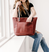 Person holding a merlot leather tote bag in a minimalistic setting