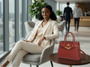 Woman in a beige suit sitting in an office with a burgundy croc leather tote handbag on a table.