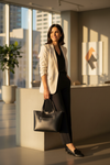 Woman in professional attire holding a black leather tote in an office setting