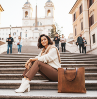 Woman sitting on steps with a brown leather tote in an urban setting
