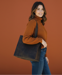 Woman carrying a dark brown leather tote in front of a dark orange background.