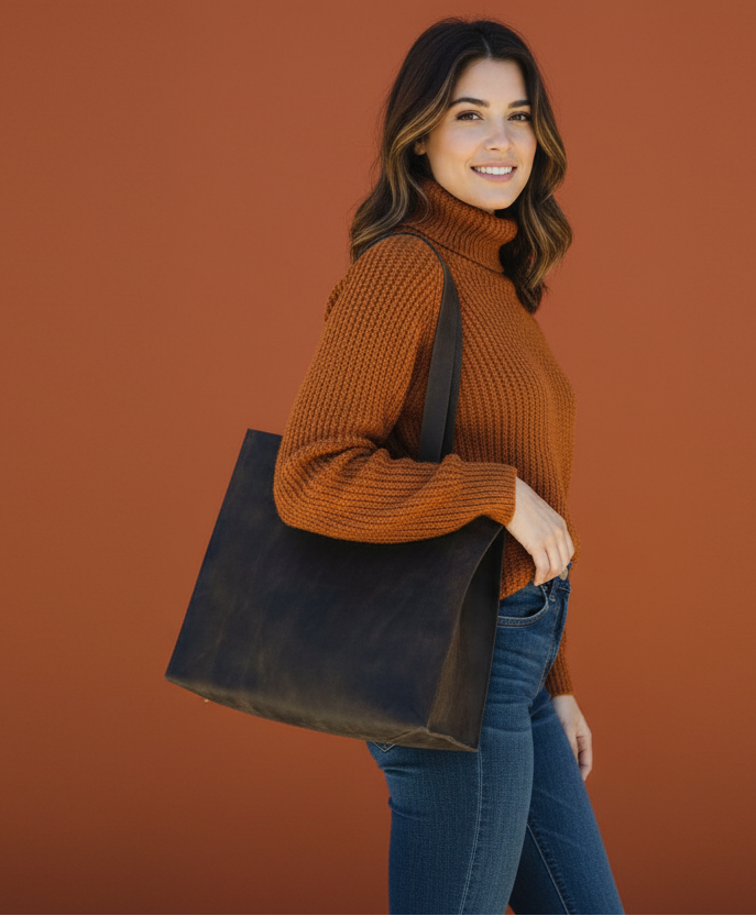 Woman carrying a dark brown leather tote in front of a dark orange background.