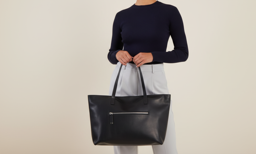 Woman holding a black tote bag against a beige background